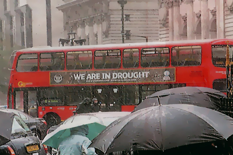 A London bus with a drought advertisement, in the rain.